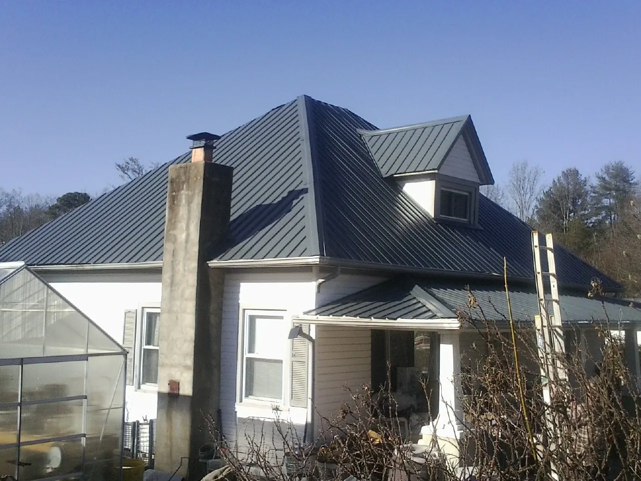 Dark blue standing seam metal roof on a white farmhouse with dormer — Slate & Tile Roof Repair by Roofing Brothers in West Friendship