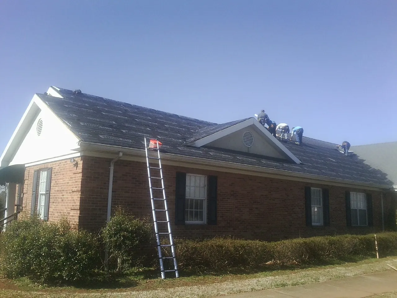 Crew tearing shingles off a brick ranch roof with a ladder set — Metal Roof Repair work by our crew in West Friendship