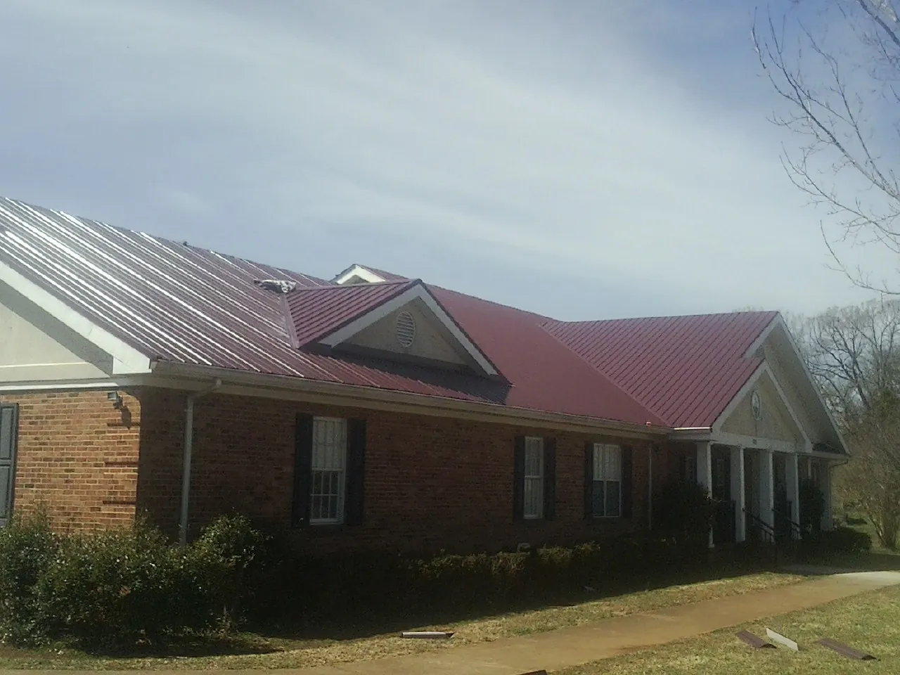 Red metal roof with gabled entries on a long brick building, from a Hail Damage Roof Repair job in West Friendship