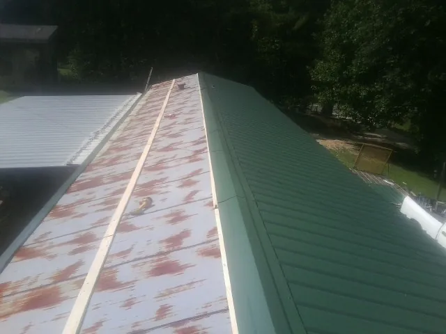 Old rusted panels beside newly installed green metal roofing — Wind Damage Roof Repair by Roofing Brothers in West Friendship