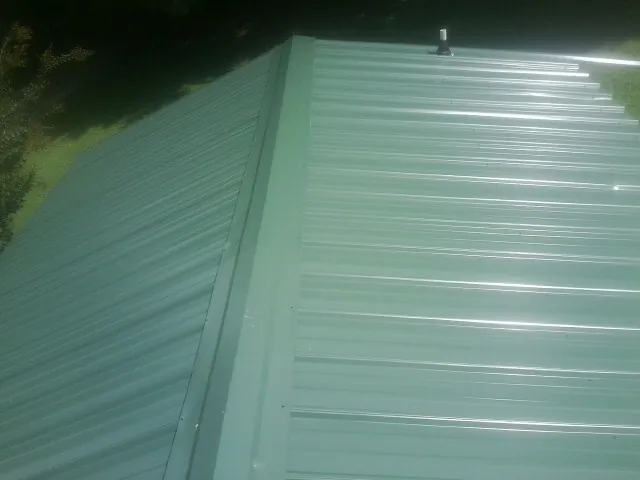 New green metal panels meeting at the ridge of a roof — Flat Roof Repair work by our crew in West Friendship