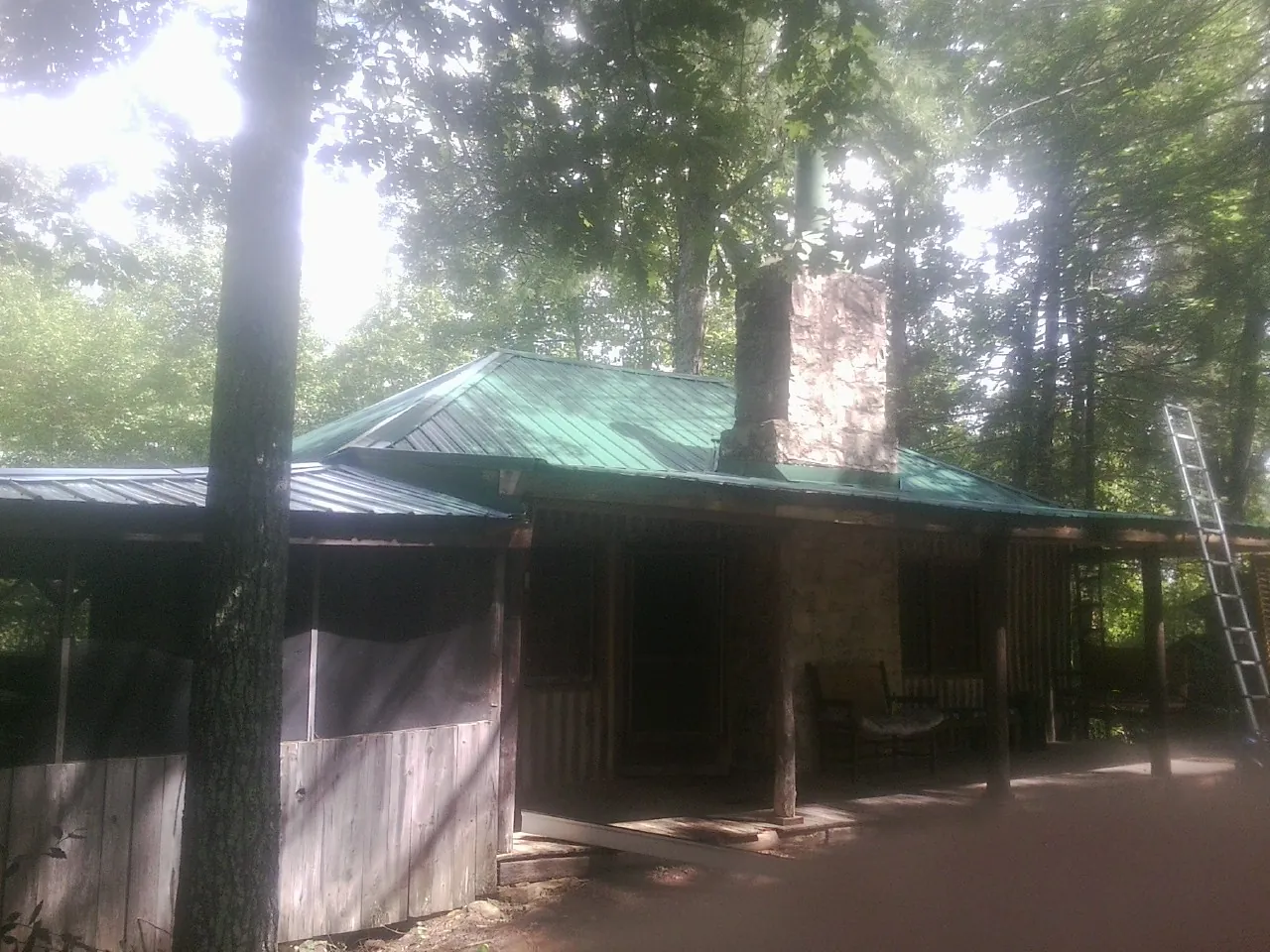Green metal roof and stone chimney above a log cabin porch in West Friendship