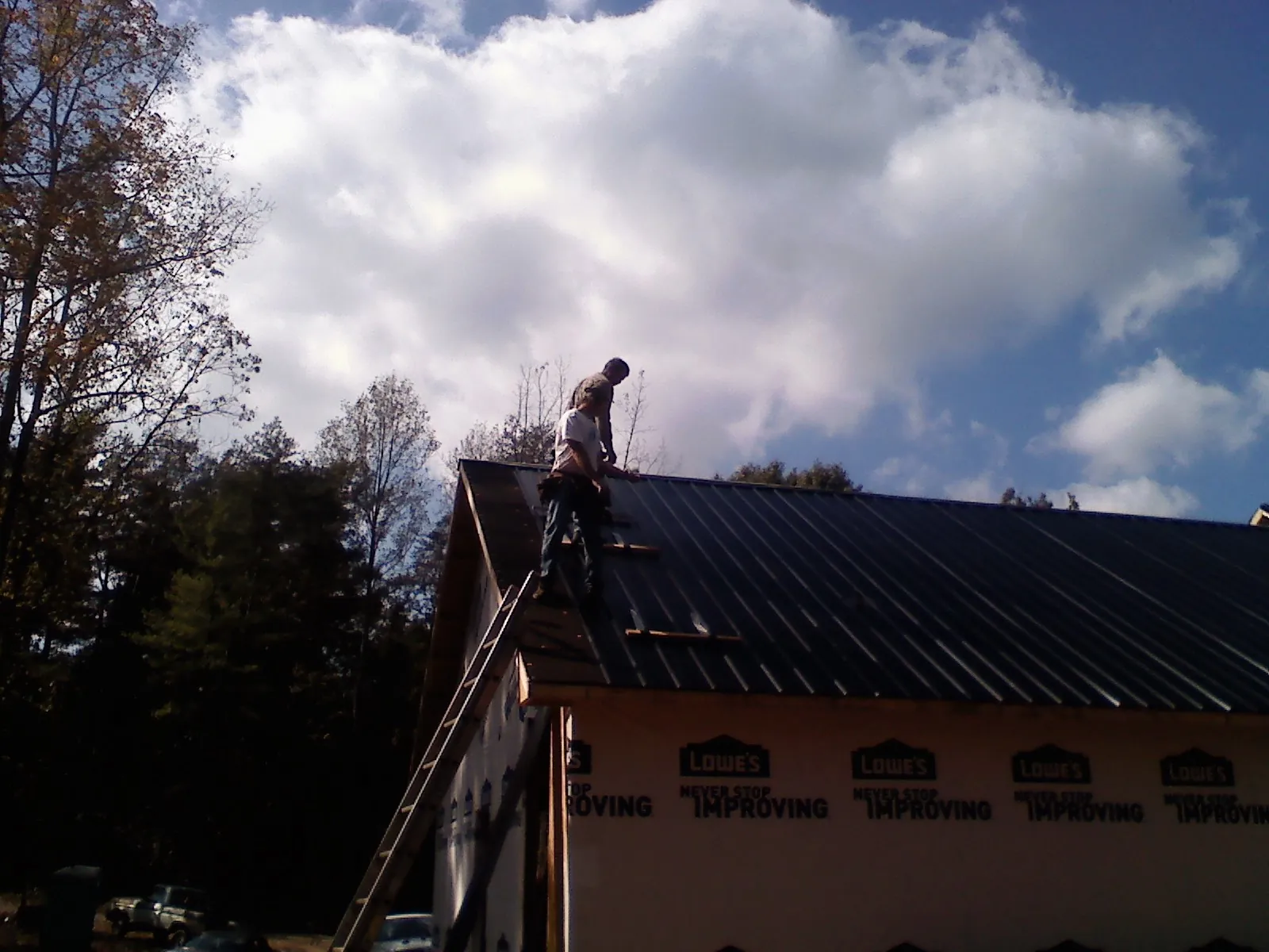 Roofer fastening dark metal panels high against a cloudy sky, from a Roof Inspection job in West Friendship