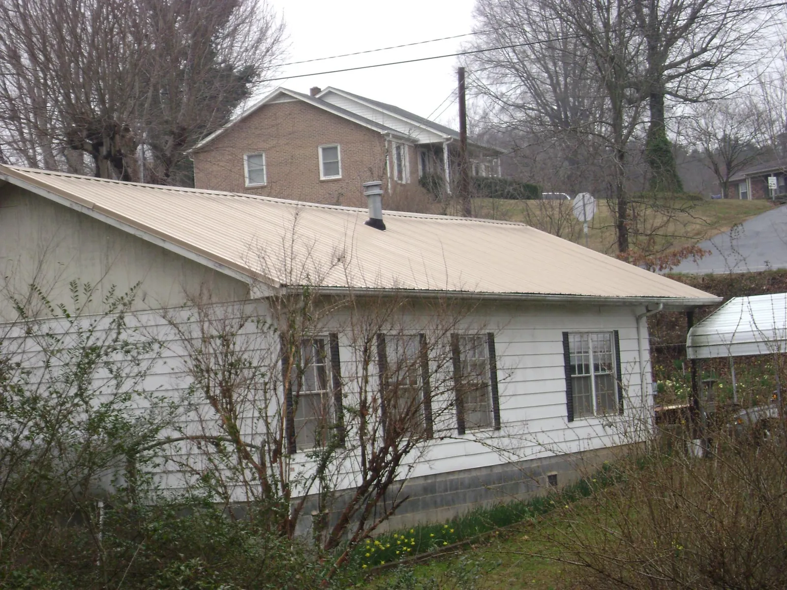Tan metal roof on a white sided house set into a hillside — Commercial Roofing by Roofing Brothers in West Friendship